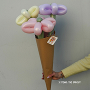 Balloon bouquet in a brown paper cone held by a person against a plain background