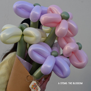 Bouquet of balloon flowers in pink, purple, and green held by a person against a plain background.